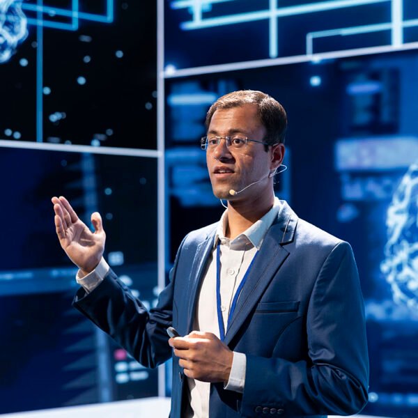 Man speaking at tech expo, exploring latest AI technology trends and case studies. Computer scientist presenting latest artificial intelligence innovations during large event